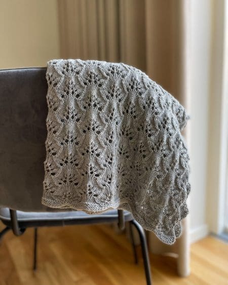 Et gråt Blueberry Baby Blanket i Bøllefrø fv. 1 Lys Grå, hænger over en grå stol i en stue.