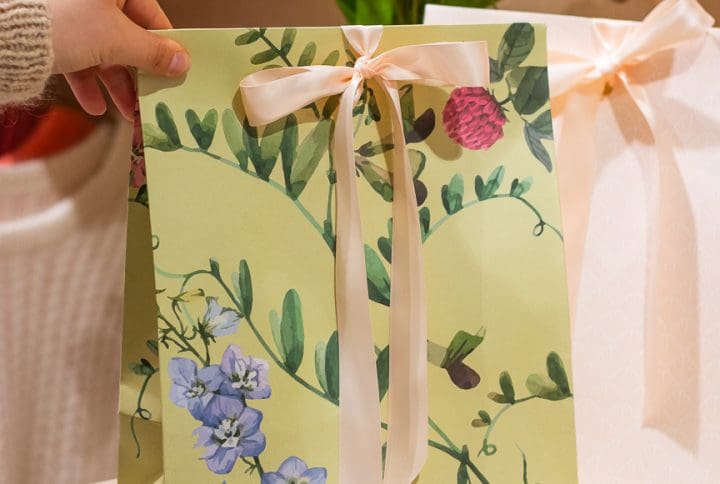 En grøn blomstret gavepose er ved at blive sat på et bord.