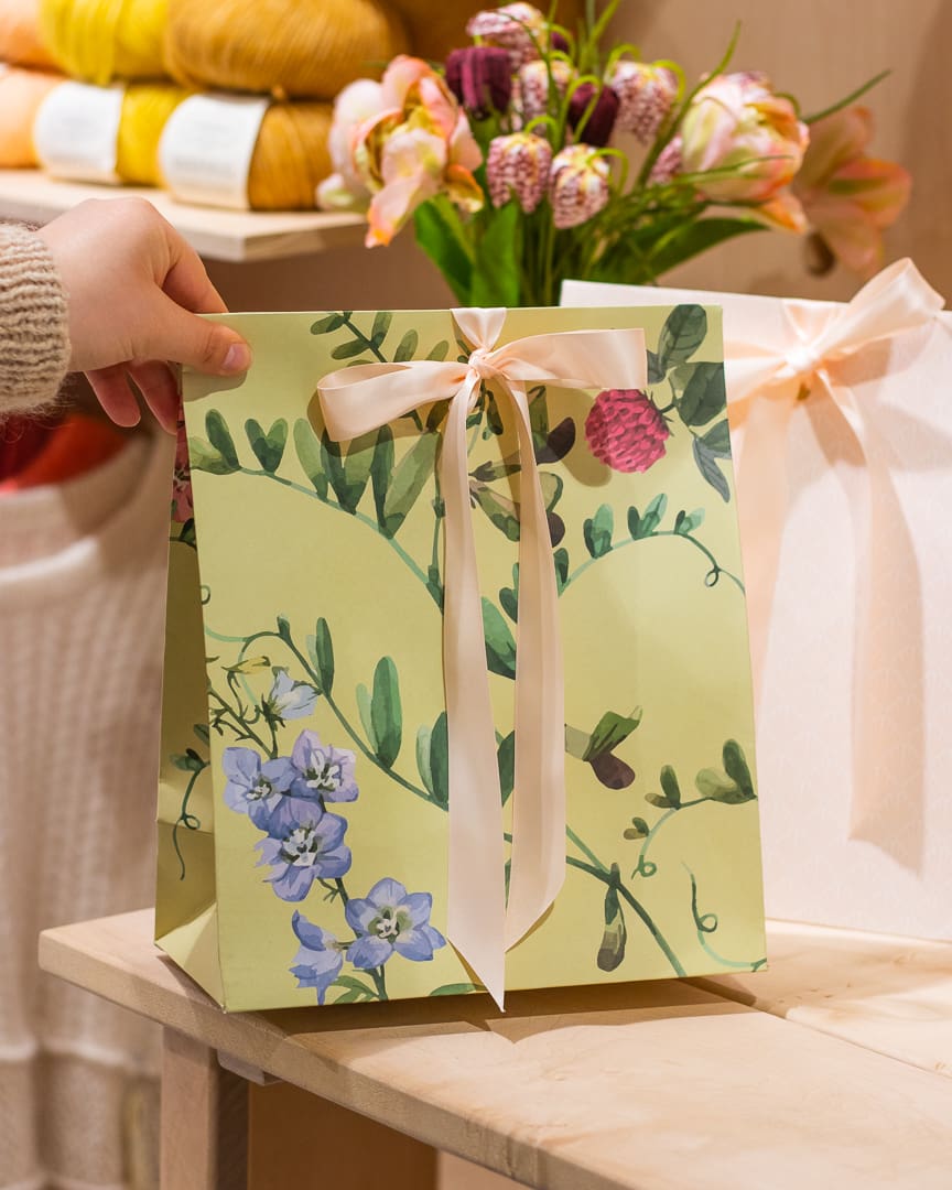 En grøn blomstret gavepose er ved at blive sat på et bord.