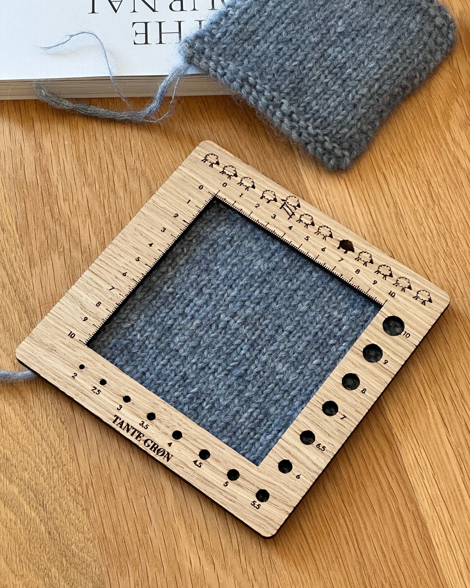 En strikkeprøve hvor strikkefastheden bliver aflæst med en strikkefasthedsmåler i træ.