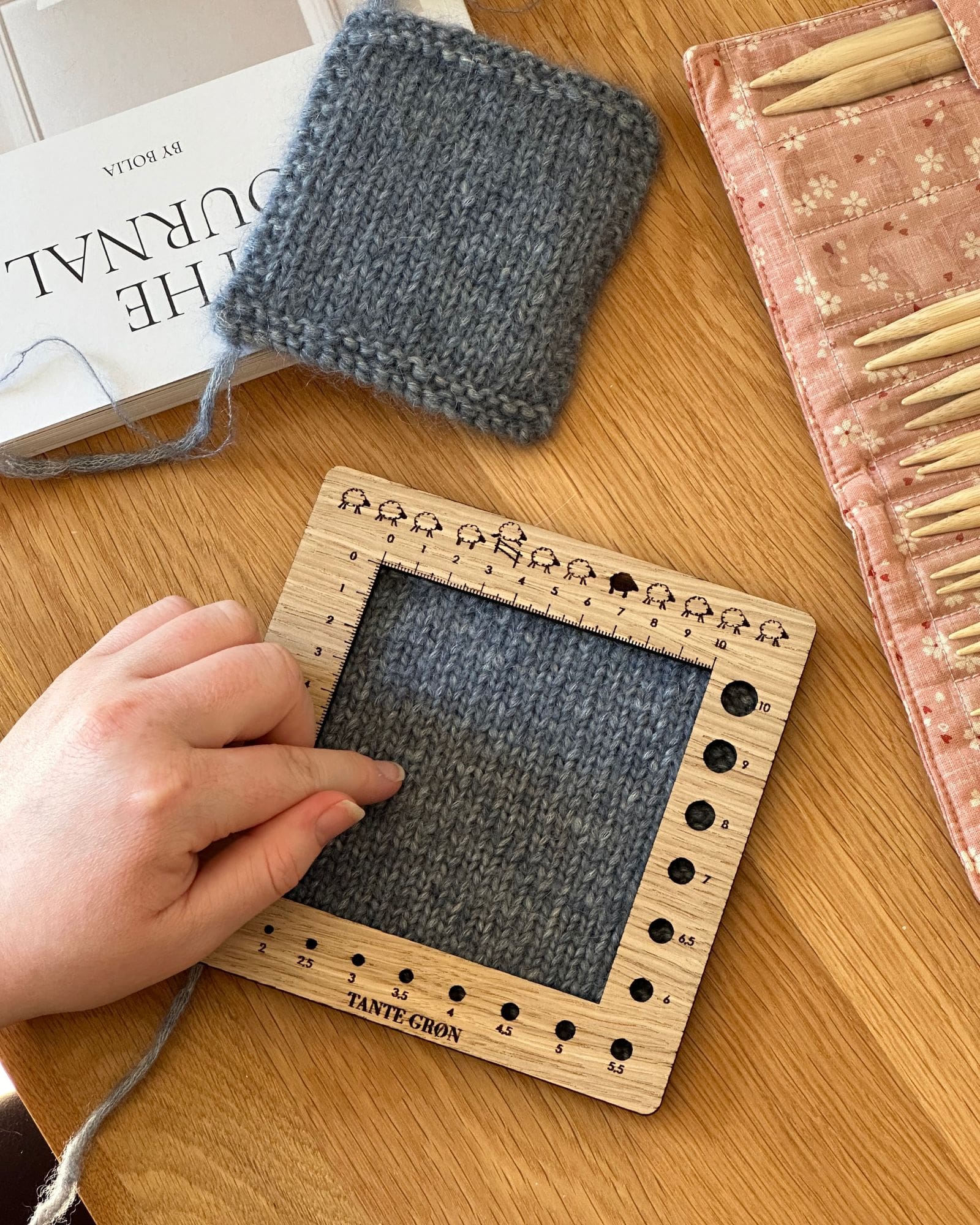 En person er ved at måle sin strikkefasthed på sin strikkeprøve, med sin strikkefasthedsmåler.