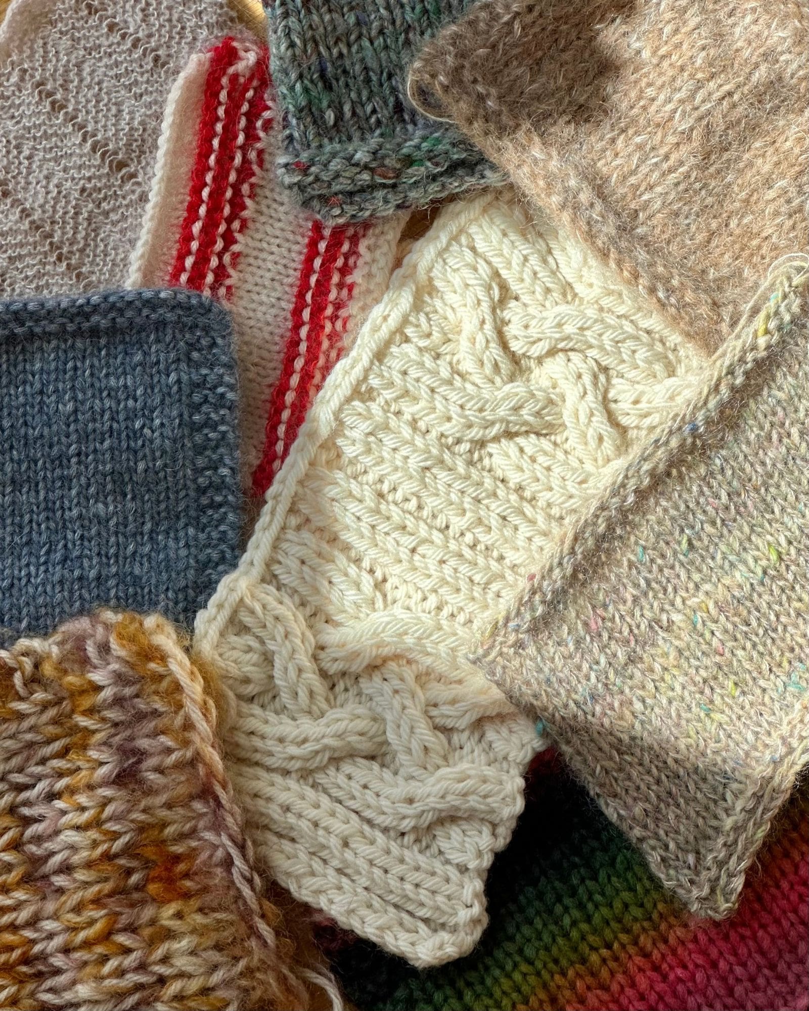 Ni forskellige strikkeprøver til at måle strikkefastheden med. De findes både i glatstrik, mønster og struktur. Forrest i billedet er en hvid strikkeprøve i strukturstrik.