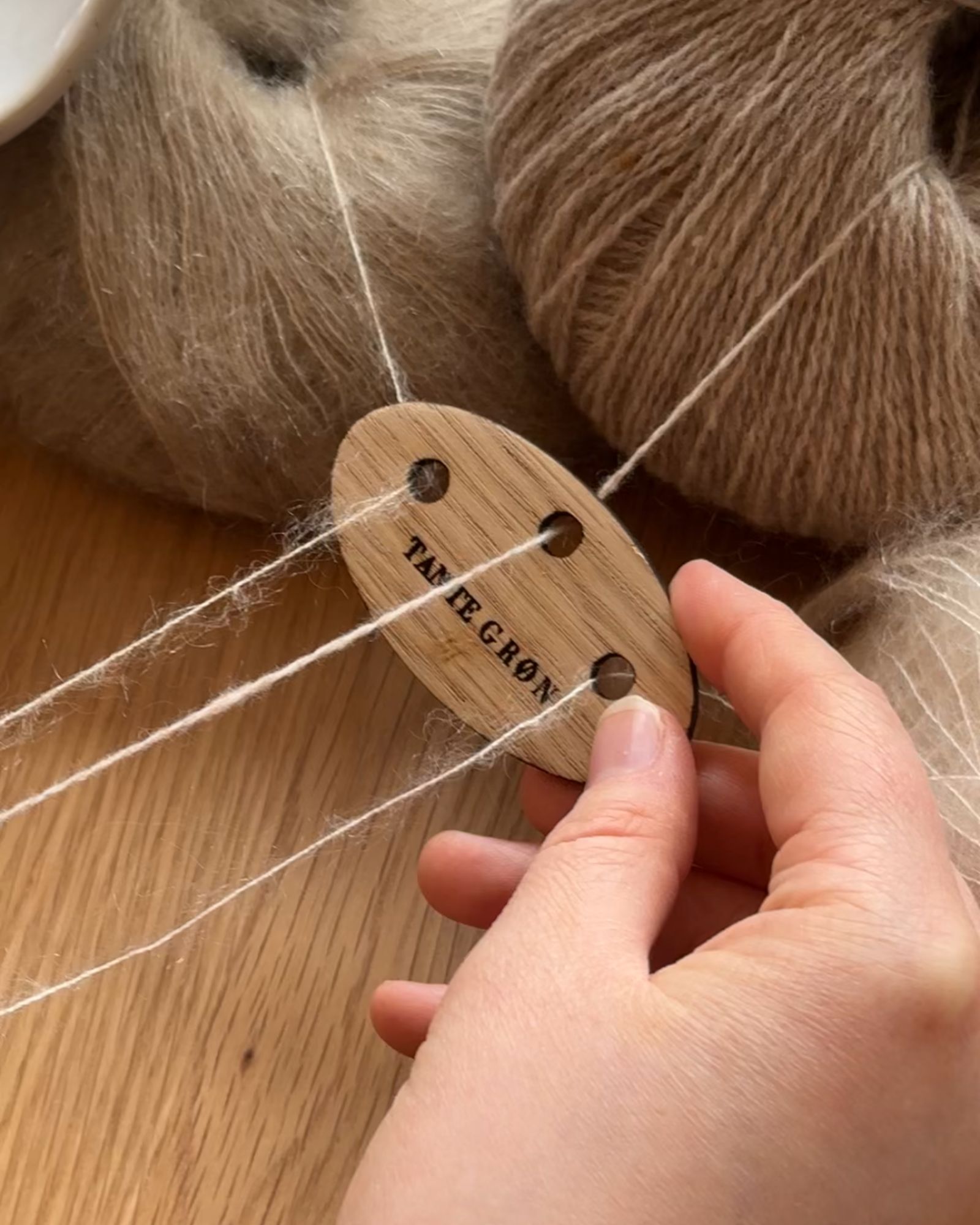 En rund tråddeler i træ med tre huller i, bliver brugt til at holde tre tråde adskilt i strikkeprocessen.