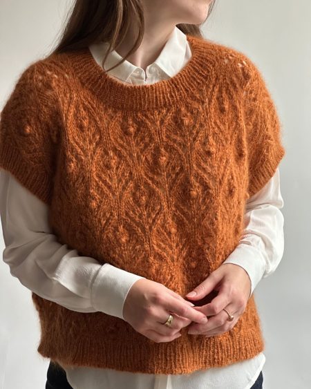 Kvinde har den strikkede Thea Slipover på, i en brændt orange farve.